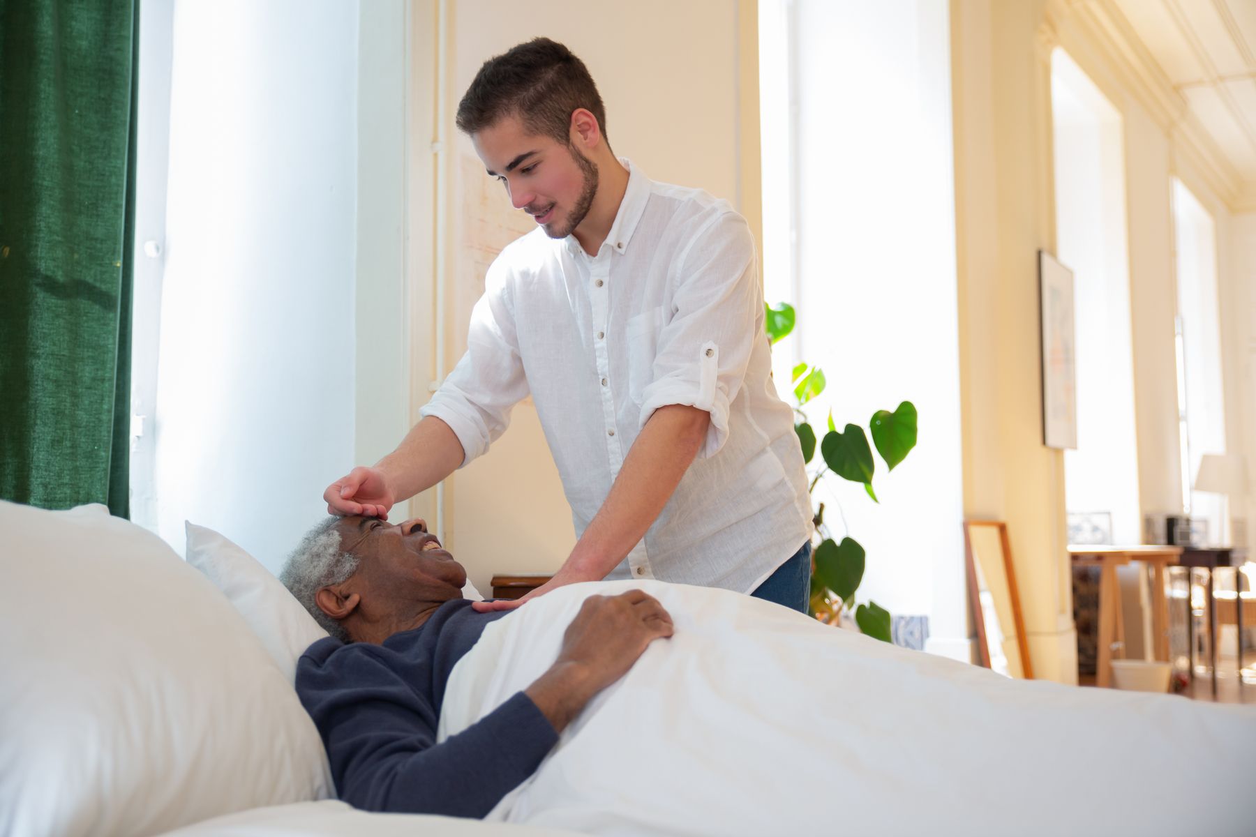 A caregiver checking in on an older man resting at home after illness