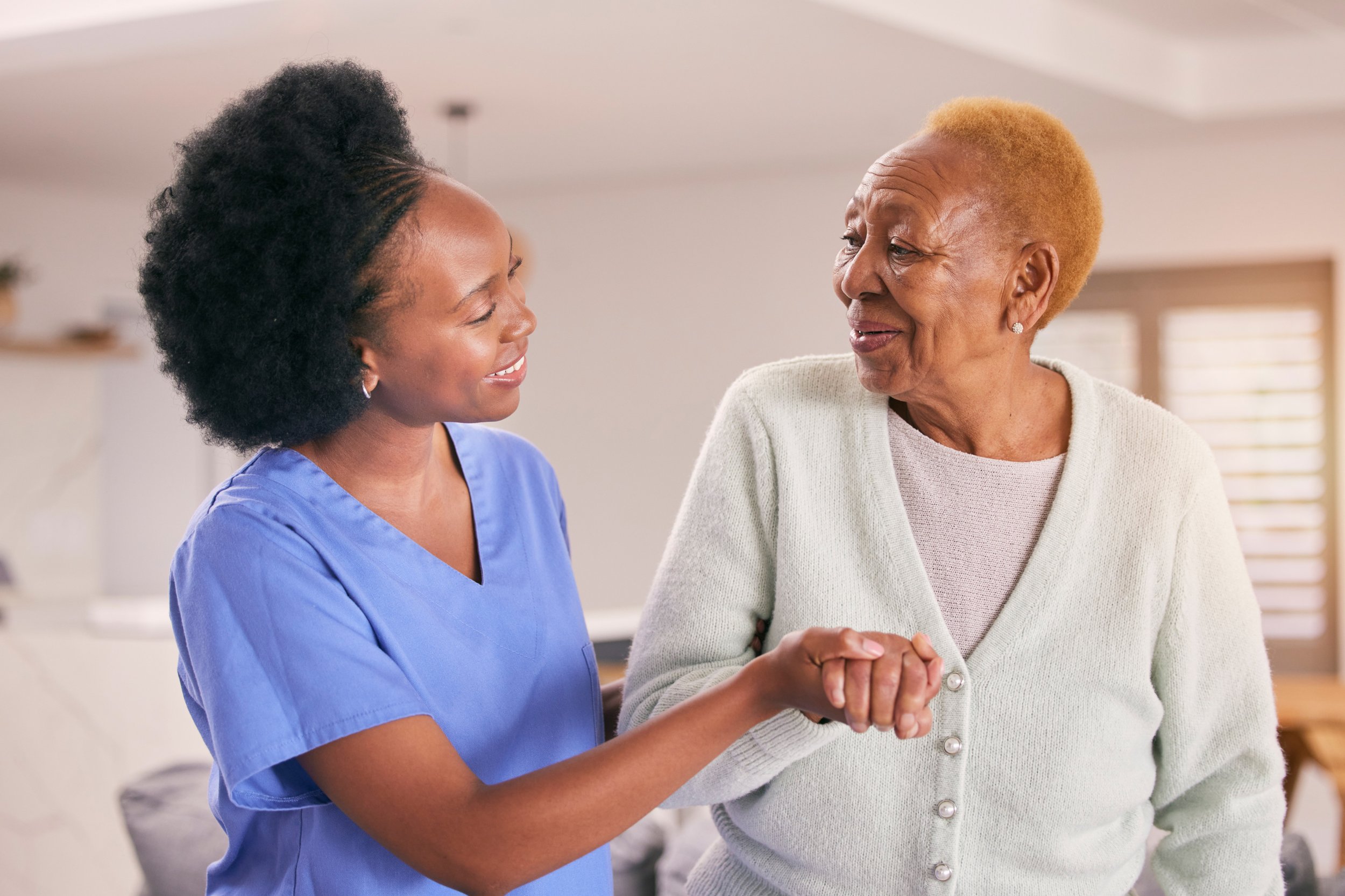 A Black caregiver holding hands with an older woman